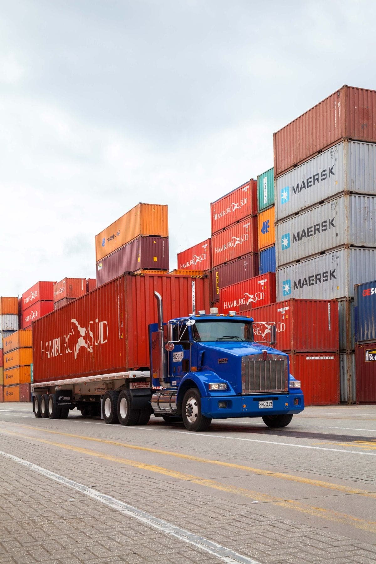 A container truck loaded and pulling away through a stacked container yard