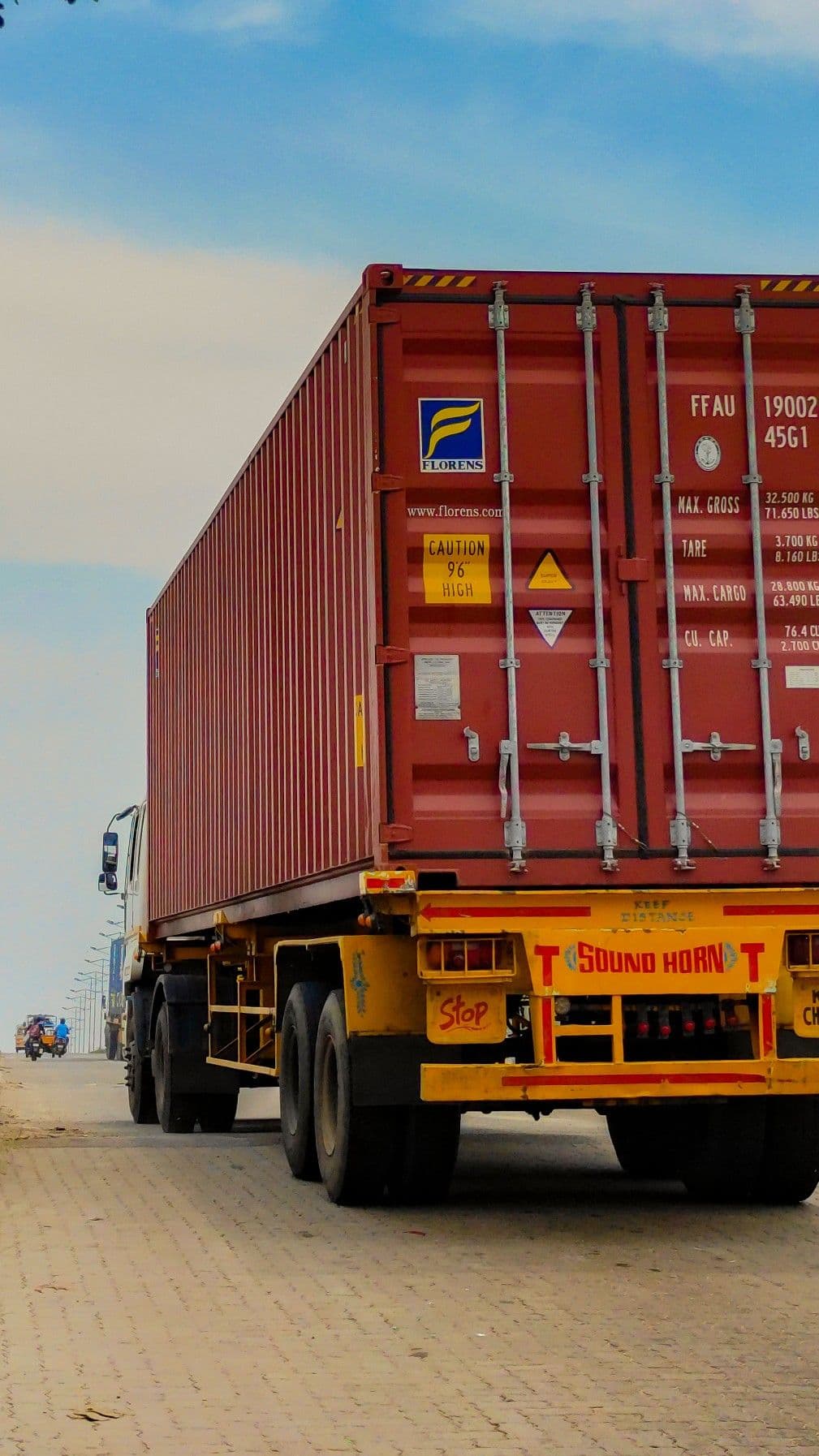 A laden forty-foot container on a flatbed trailer, seen from behind on the road