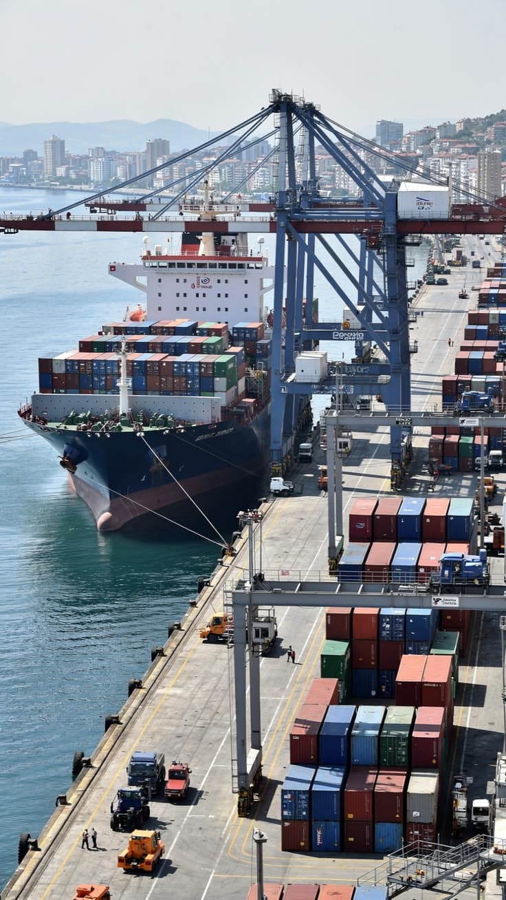 High-angle view of a container ship docked at a busy port with large blue gantry cranes
